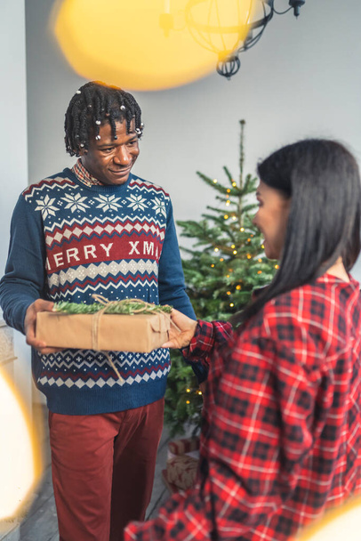 vertical shot of a cute couple exchanging gifts in front of a Christmas tree. High quality photo - Foto, imagen