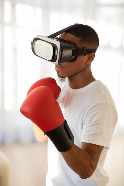 仮想メタバース拡張現実。VRヘッドセットでボクシングを行う運動黒男の肖像,リビングルームのインテリアで仮想現実でボクシングパンチのためのトレーニング,垂直ショット - 写真・画像