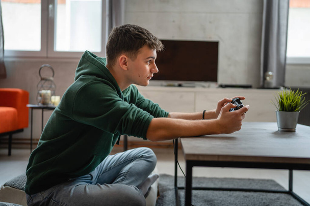 Ένας έφηβος καυκάσιος νεαρός άνδρας παίζει κονσόλα βιντεοπαιχνίδι στο σπίτι - Φωτογραφία, εικόνα