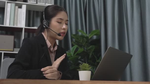Businesswoman wearing headset and microphone working at her desk and using laptop. Enthusiastic female employee utilizing laptop for remote online meeting, business video conference in the office. - Imágenes, Vídeo