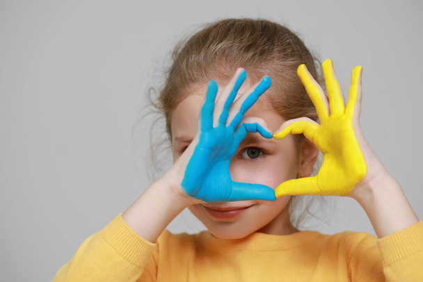 Little girl making heart with her hands painted in Ukrainian flag colors on light grey background, space for text. Love Ukraine concept - Photo, Image
