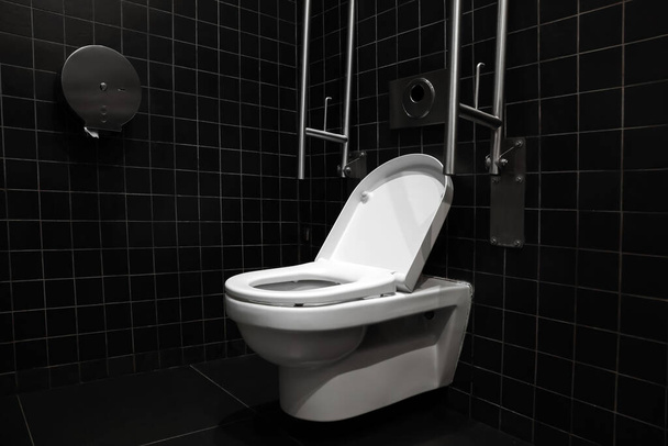 Clean ceramic toilet bowl and handrails on tiled wall indoors - Φωτογραφία, εικόνα