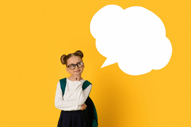 Pensive Cute Schoolgirl In Eyeglasses Looking At Blank Speech Bubble While Standing Isolated Over Yellow Studio Background, Thoughtful Female Child Having Idea, Considering Options, Mockup - Photo, Image