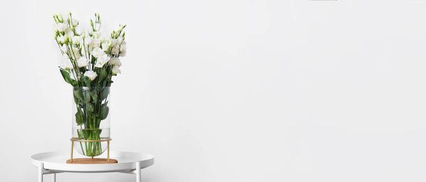 Vase with beautiful eustoma flowers on table near light wall. Banner for design - Photo, Image