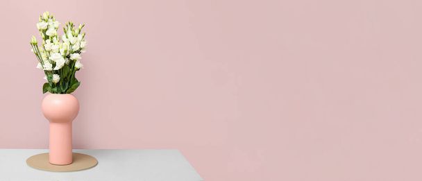 Ваза с букетом красивых цветов эустомы на столе возле розовой стены. Баннер для дизайна - Фото, изображение