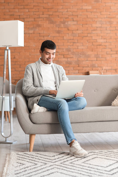 Giovane uomo che utilizza il computer portatile sul divano grigio a casa - Foto, immagini