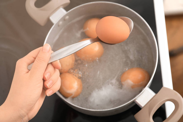 Woman holding spoon with boiled egg above cooking pot in kitchen, closeup - Фото, изображение