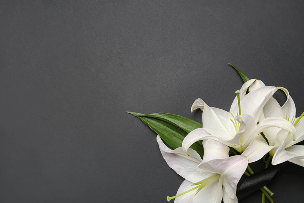 Białe kwiaty lilii i czarna wstążka pogrzebowa na ciemnym tle - Zdjęcie, obraz