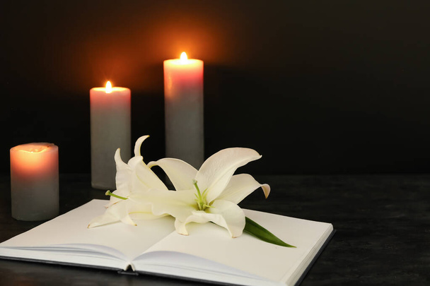 Open book, white lily flowers and burning candles on dark background - Foto, Imagen