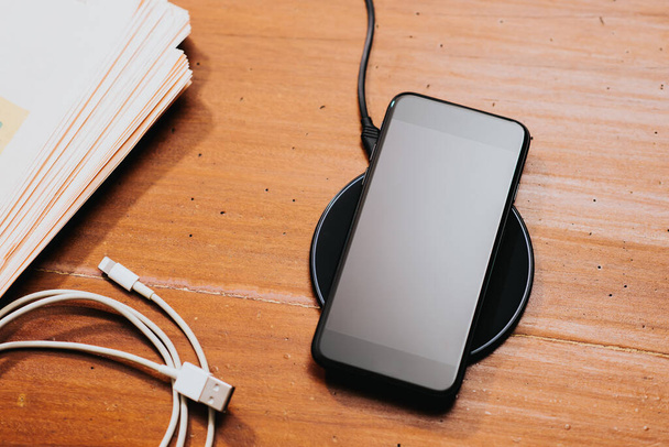 Charging the smartphone with wireless charger on desktop. - Foto, Imagen