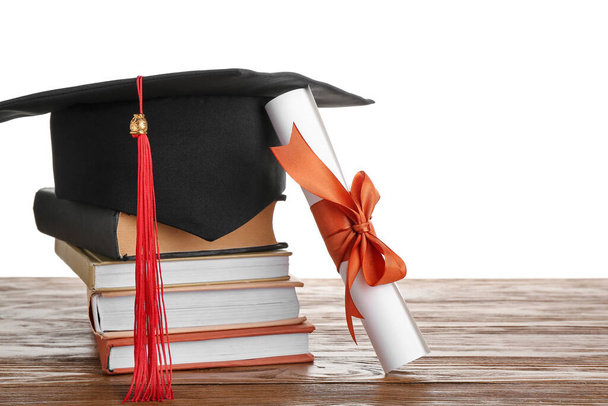 Graduation hat with diploma and books on wooden table against white background - Foto, Imagem