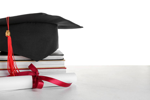 Graduation hat with diploma and books on table against white background - Foto, imagen