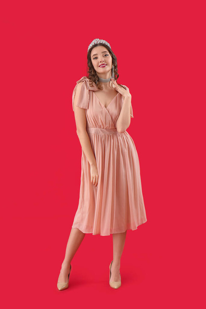 Beautiful young woman in prom dress and tiara on red background - Valokuva, kuva