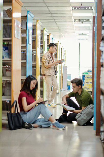 Grupa studentów siedząca na podłodze biblioteki - Zdjęcie, obraz