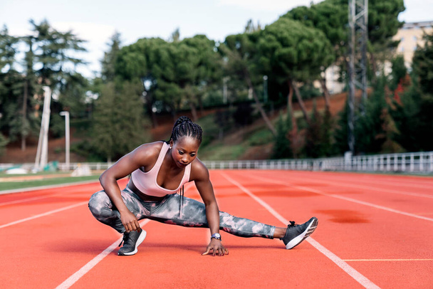 Stock photo of an African-American sprinter stretching her legs before training - Foto, Imagem