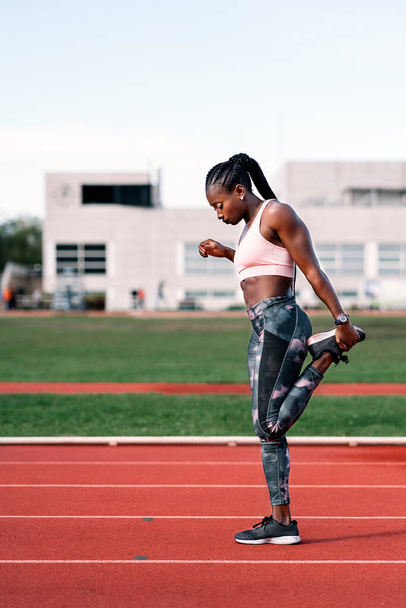 Stock photo of an African-American sprinter stretching her legs before training - Fotografie, Obrázek