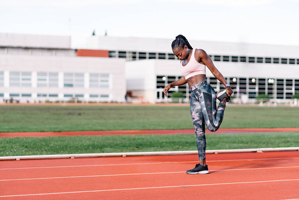 Stock photo of an African-American sprinter stretching her legs before training - Foto, Bild