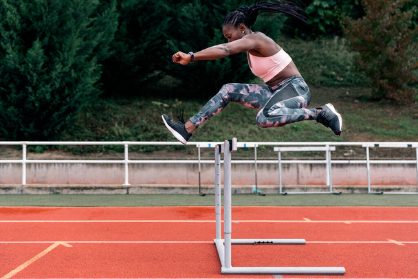 Stock photo of an African-American sprinter jumping a hurdle in the sports center - Photo, image