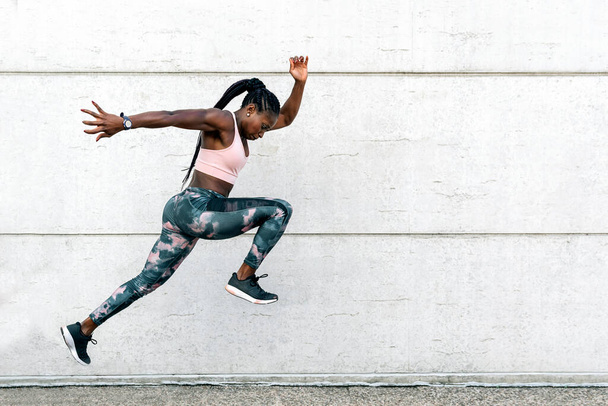 Stock photo of an African-American sprinter jumping in front of a clear wall - Foto, Imagem