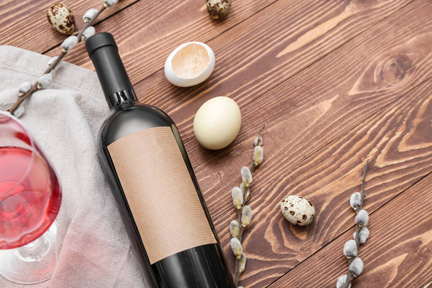 Composición con botella de vino, copa, huevos de Pascua y ramas de sauce sobre fondo de madera, primer plano - Foto, imagen