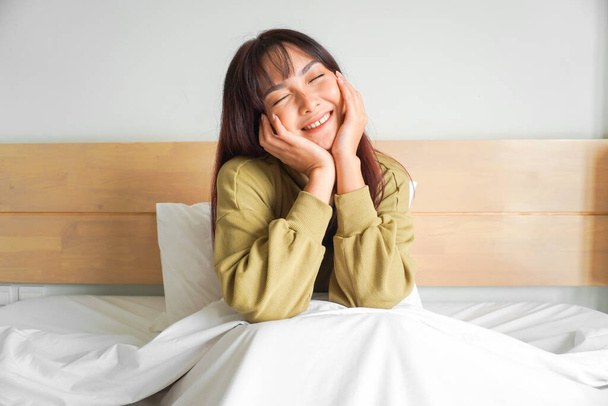 Una joven asiática feliz sonríe mientras está sentada en la cama - Foto, imagen