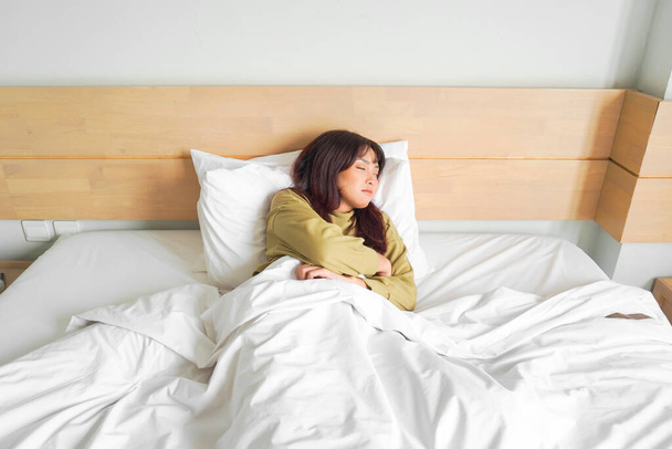 Young beautiful Asian woman sleeping in her bed and relaxing in the morning - Photo, image