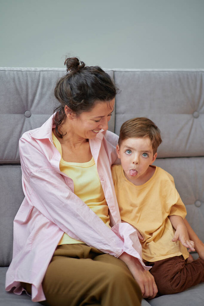 Retrato de una mujer caucásica jugando con un niño pequeño sentado en un sofá en casa. Concepto de tiempo familiar juntos. Foto vertical de alta calidad - Foto, imagen