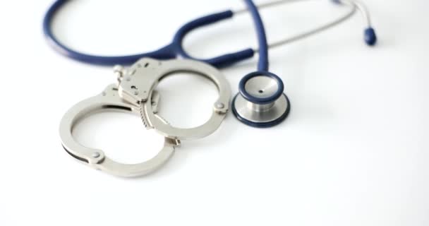 Handboeien en medische stethoscoop op witte achtergrond close-up. Omkoping van medische misdrijven en corruptie in de gezondheidszorg - Video