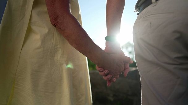 Ältere Eheleute hielten die Hände im Freien bei strahlendem Sonnenschein zusammen. Nahaufnahme von verliebten und unterstützten älteren Menschen - Foto, Bild