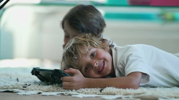 Portrait of joyful child holding tablet device lying on floor turning head to camera smiling. Kids close up face posing - Fotoğraf, Görsel