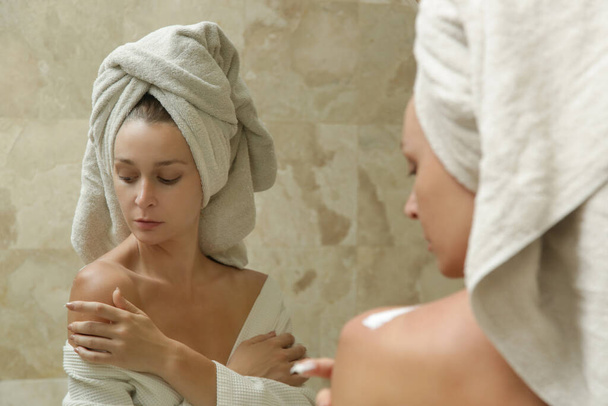 Woman applying body lotion to moisturize her skin after shower, beauty skin care concept - Photo, Image