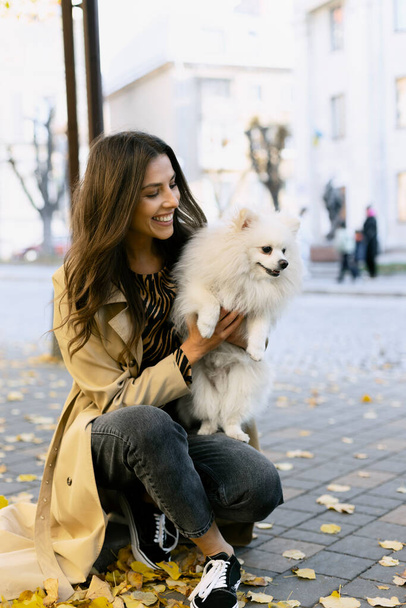 Alegre, joven niña sostiene un hermoso perro en sus brazos, en la calle. Chica sonriente sosteniendo a su mascota, hojas caídas, otoño. - Foto, Imagen