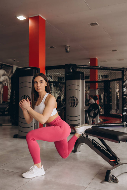Pretty concentrated young sportswoman doing squats using bench in gym - Photo, image