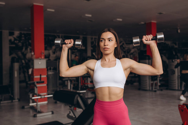 М'язиста молода фітнес спортивна жінка тренується з гантелями у фітнес-залі
. - Фото, зображення