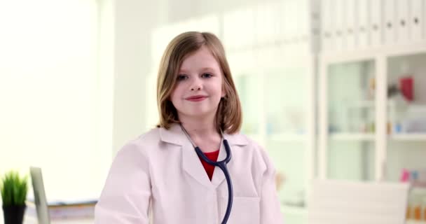 Muotokuva kaunis pieni tyttö stetoskooppi lääkärin takki. Sairausvakuutus ja koulutus - Materiaali, video