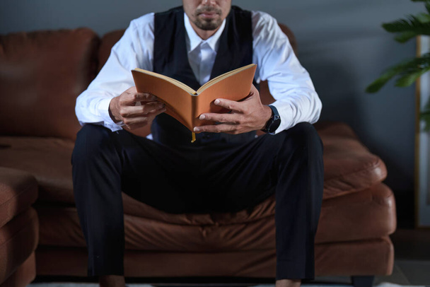 Портрет доброго азіатського чоловіка, який сидить на дивані і читає книжку.. - Фото, зображення