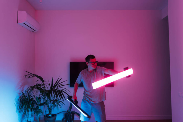 Mid adult man funny with led neon laser at home, samurai or Jedi. High quality photo - Foto, afbeelding