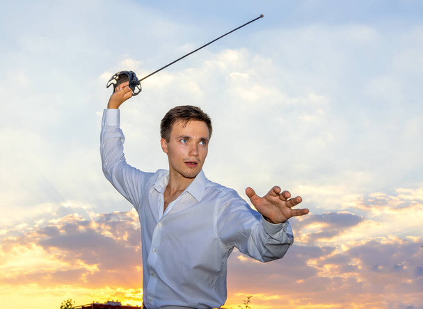 A man with a rapier in his hands, against the backdrop of the sunset sky. Young warrior. - Foto, immagini