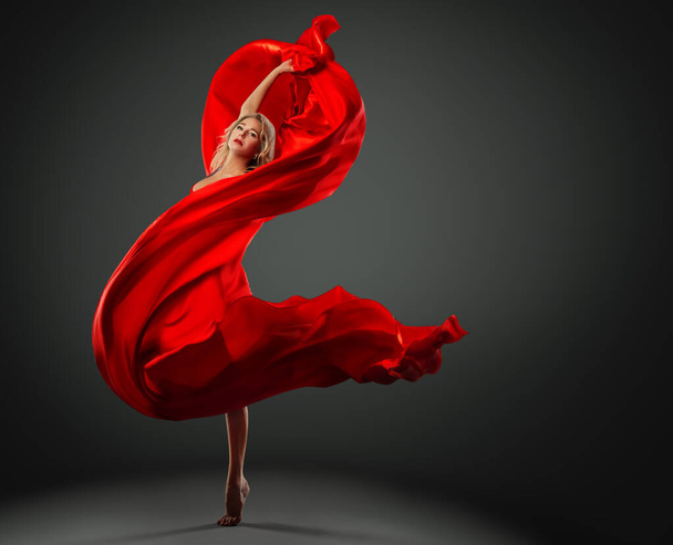 Ballerina dancing with Red Silk Fabric flying on Wind. Modern Ballet Dancer jumping over Dark Studio background. Fashion Woman in Red Dress wrapped in waving Scarf - Foto, Imagen
