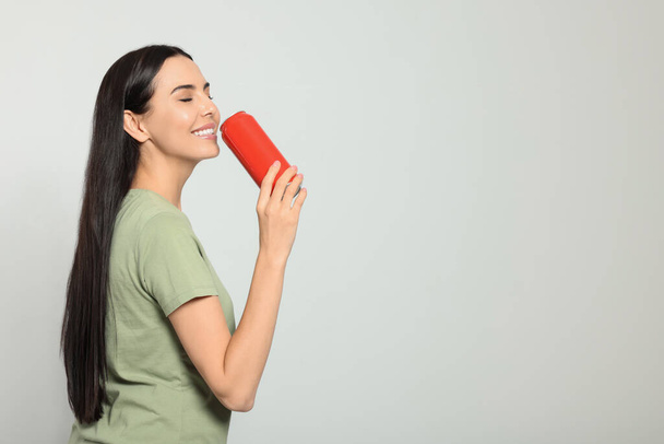 Beautiful happy woman holding red beverage can on light grey background. Space for text - Fotó, kép