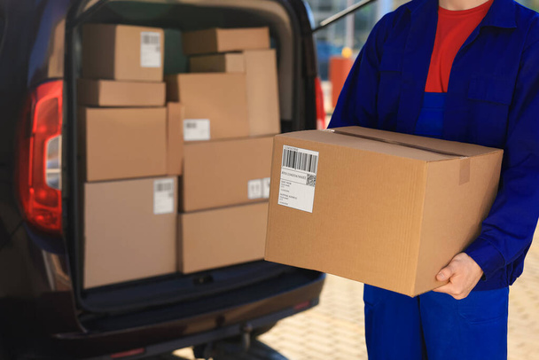 Courier with parcel near delivery van outdoors, closeup. Space for text - 写真・画像