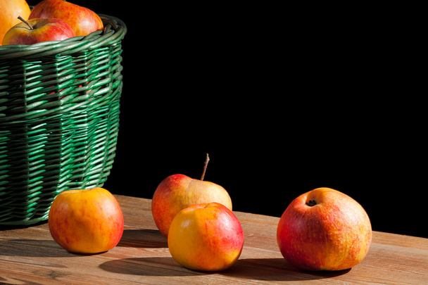 Apples in basket on old plank on black background - Foto, afbeelding