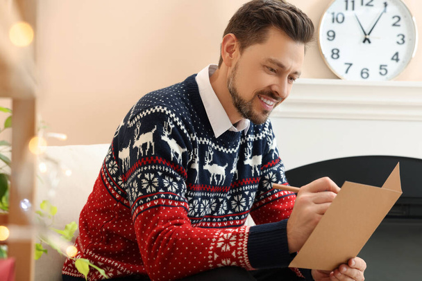 Happy man writing wishes in Christmas greeting card in living room - Foto, immagini