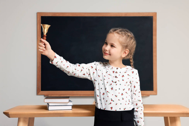Pupil with school bell near desk and chalkboard in classroom - Photo, Image