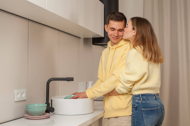 Šťastný pár ve žlutém oblečení líbání navzájem a mytí nádobí - Fotografie, Obrázek