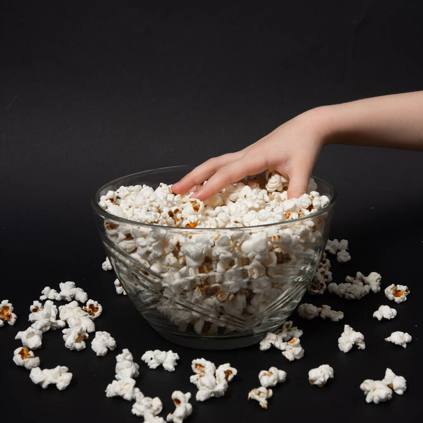 la mano di un bambino su uno sfondo nero prende i popcorn da una ciotola, popcorn appena fatti per i bambini. - Foto, immagini