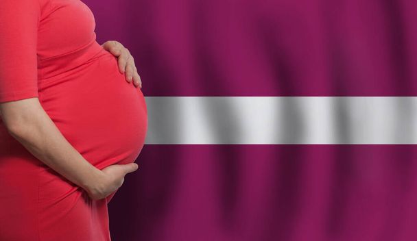 Zwangere vrouw buik op Letse vlag achtergrond - Foto, afbeelding