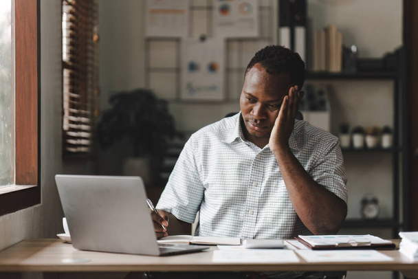ストレスにさらされたアフリカ系アメリカ人のビジネスマンは、多くの書類書類を扱っています。片頭痛の発作。フリーランス、自宅から仕事. - 写真・画像
