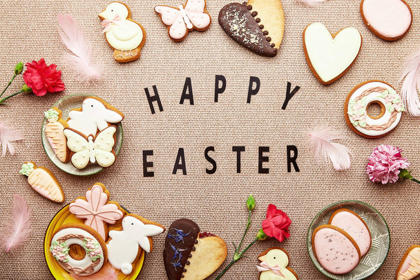 テキストとハッピーイースター春の背景。審美的なイースタークッキー、ピンクの花や卵のフラットレイ - 写真・画像