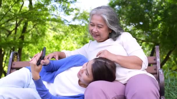 Happy senior mother with gray hair talk and laugh with daughter or caregiver in the park. Concept of happy retirement with care from a caregiver and Savings and senior health insurance, senior care - Materiał filmowy, wideo